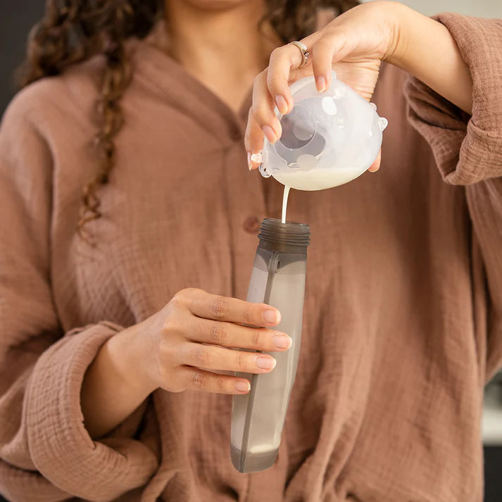 Person pouring a liquid from a small container into a clear bottle.