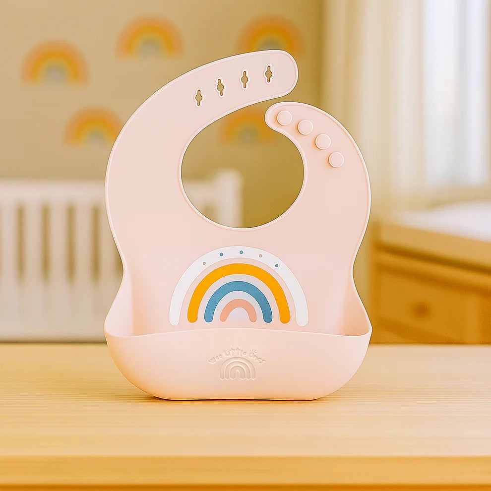 Pink silicone bib with rainbow print and adjustable button closures.