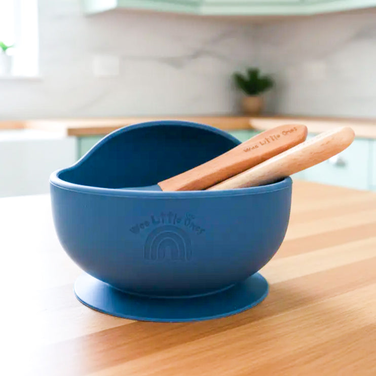 Navy blue silicone bowl with suction base and wooden utensils resting inside on a kitchen counter.