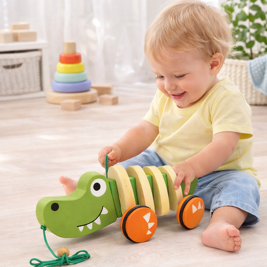 Child playing with a wooden toy alligator in a room with other toys.