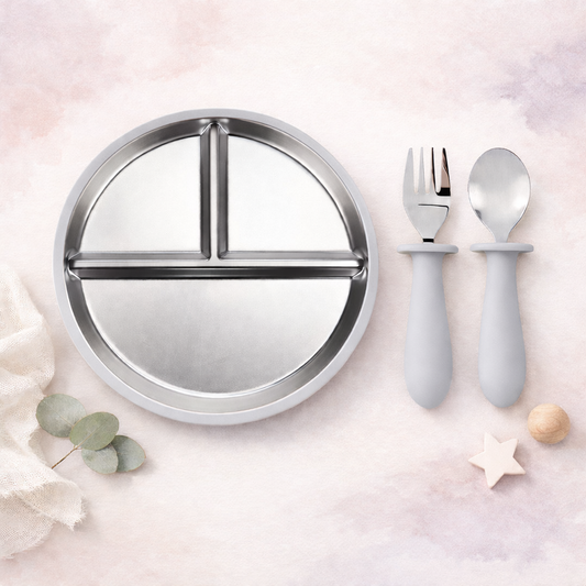 Round stainless steel plate with compartments and gray utensils on a light pink background