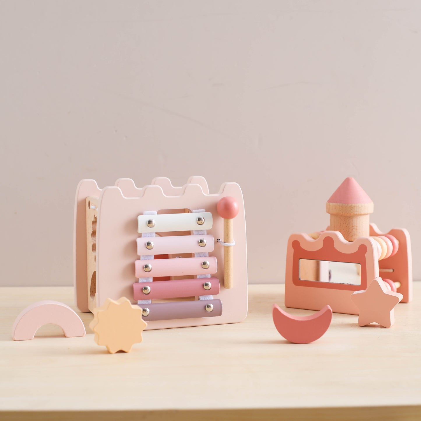 Wooden pink princess castle toy set with xylophone, mallet, and geometric shapes on light table.