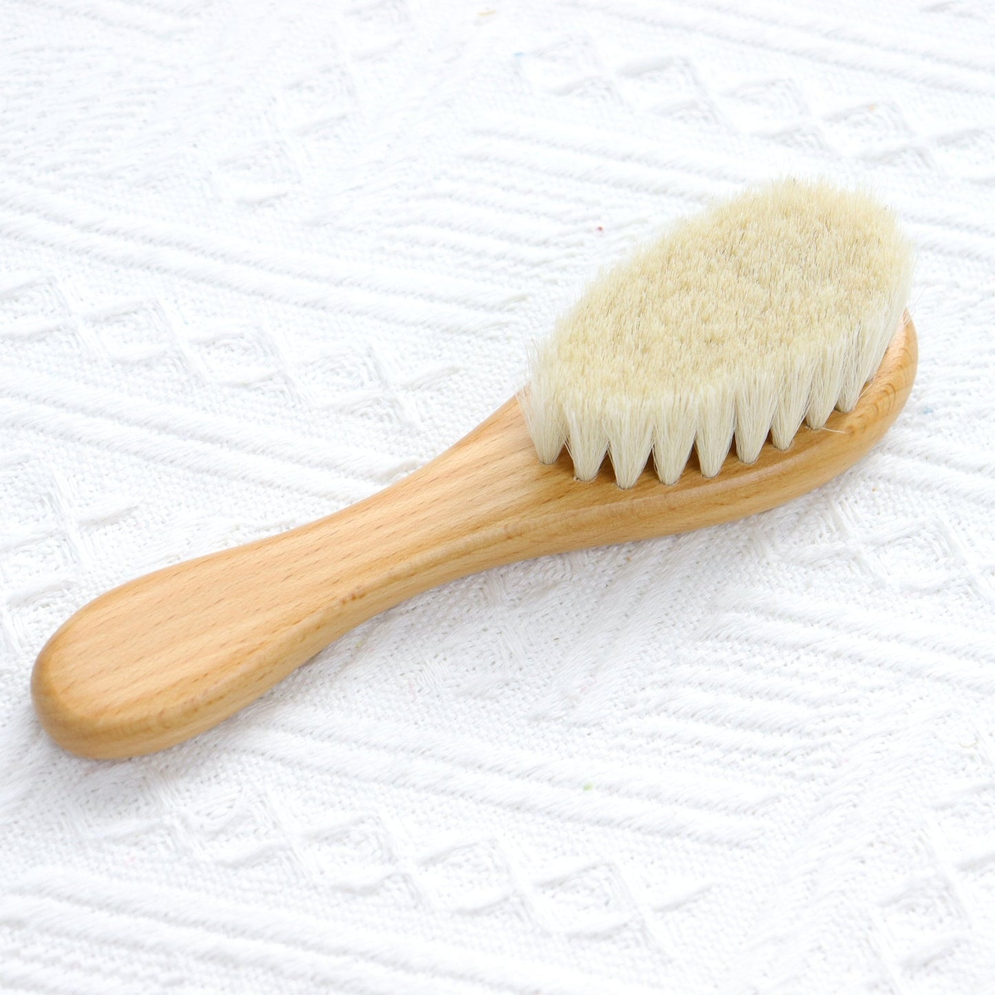 Wooden hairbrush with light-colored bristles and smooth rounded handle on white textured fabric.