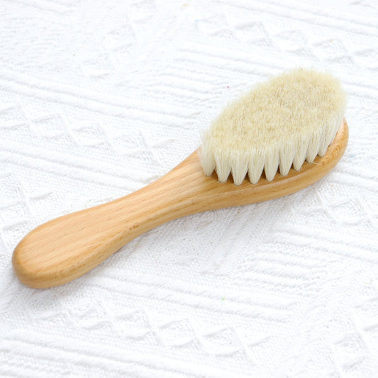 Wooden hairbrush with light-colored bristles and smooth rounded handle on white textured fabric.