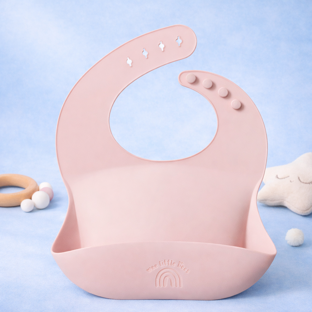 Pink silicone bib on a light blue background with baby toys.