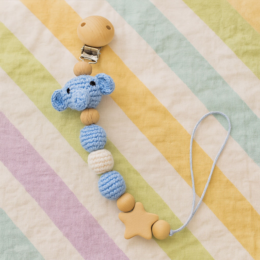 Blue crochet elephant pacifier clip with wooden beads and star-shaped charm on pastel striped background.