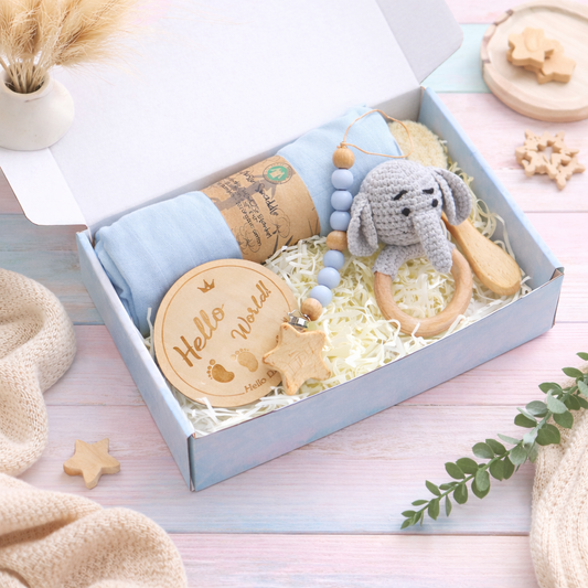 Baby gift set with toys and blanket in a box on a light wooden surface.