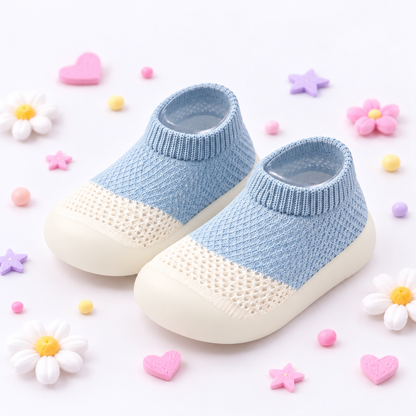 A pair of baby slip-on knit socks with light blue and cream knit uppers and cream soles, styled on a white background with decorative pastel flowers and hearts.