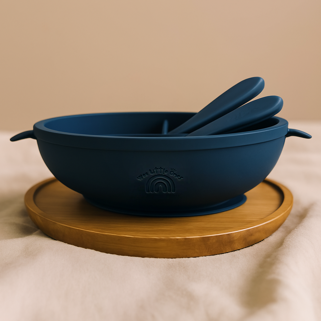 Navy blue silicone divided baby plate with matching spoon and fork on a round wooden tray.