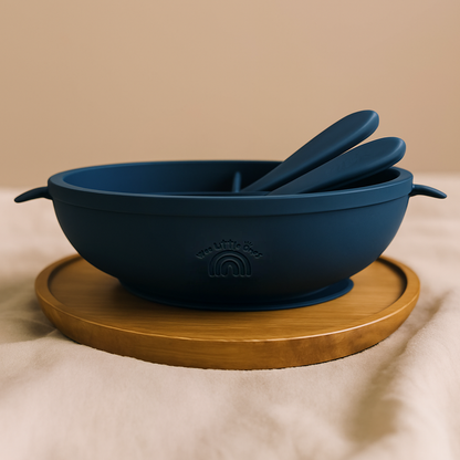 Navy blue silicone divided baby plate with matching spoon and fork on a round wooden tray.