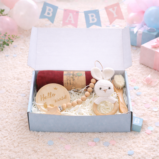 Baby gift set with toys and items in a box, surrounded by confetti and baby-themed decorations.