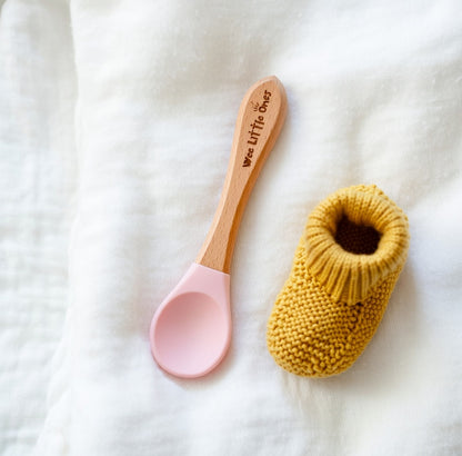 Pink baby spoon and yellow knitted item on a white background