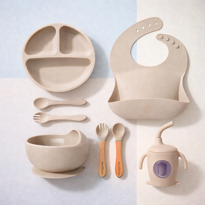 Beige baby dining set including plate, bowl, cup, spoons, and bib on a light background
