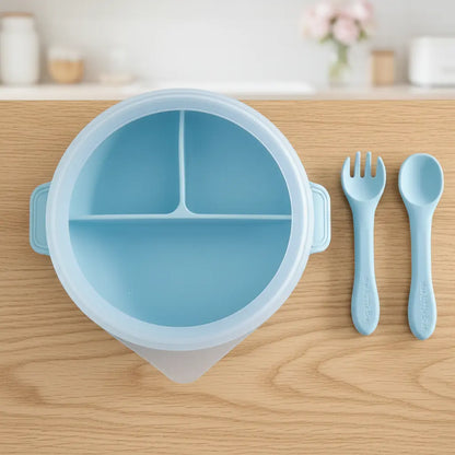 Baby blue round silicone divided plate with matching spoon and fork on wooden surface.