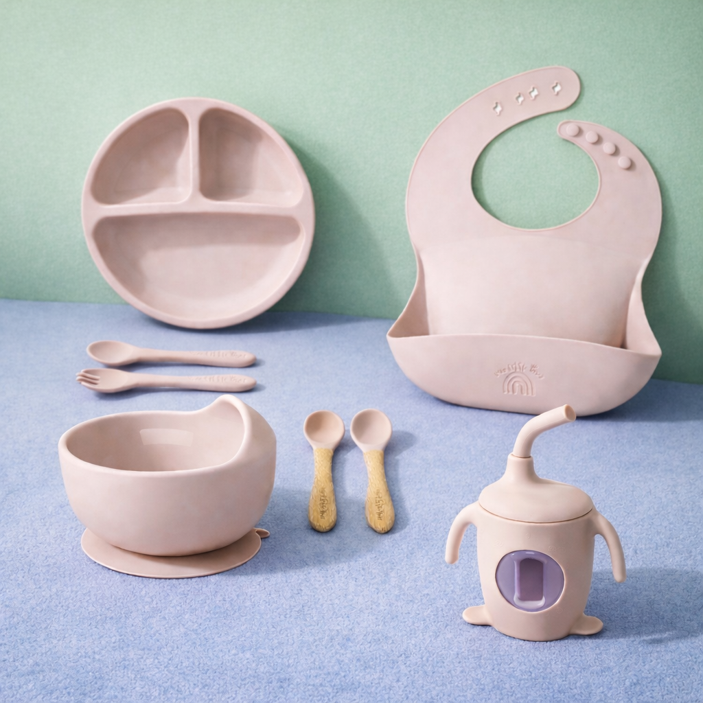 Children's dining set including a plate, bowl, sippy cup, and bib on a blue surface with a green background.