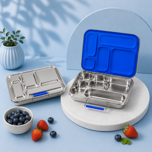 Two stainless steel compartment lunch boxes with bright blue lids are displayed on a light blue studio set. One box is closed and the other is open, showing the interior compartments.