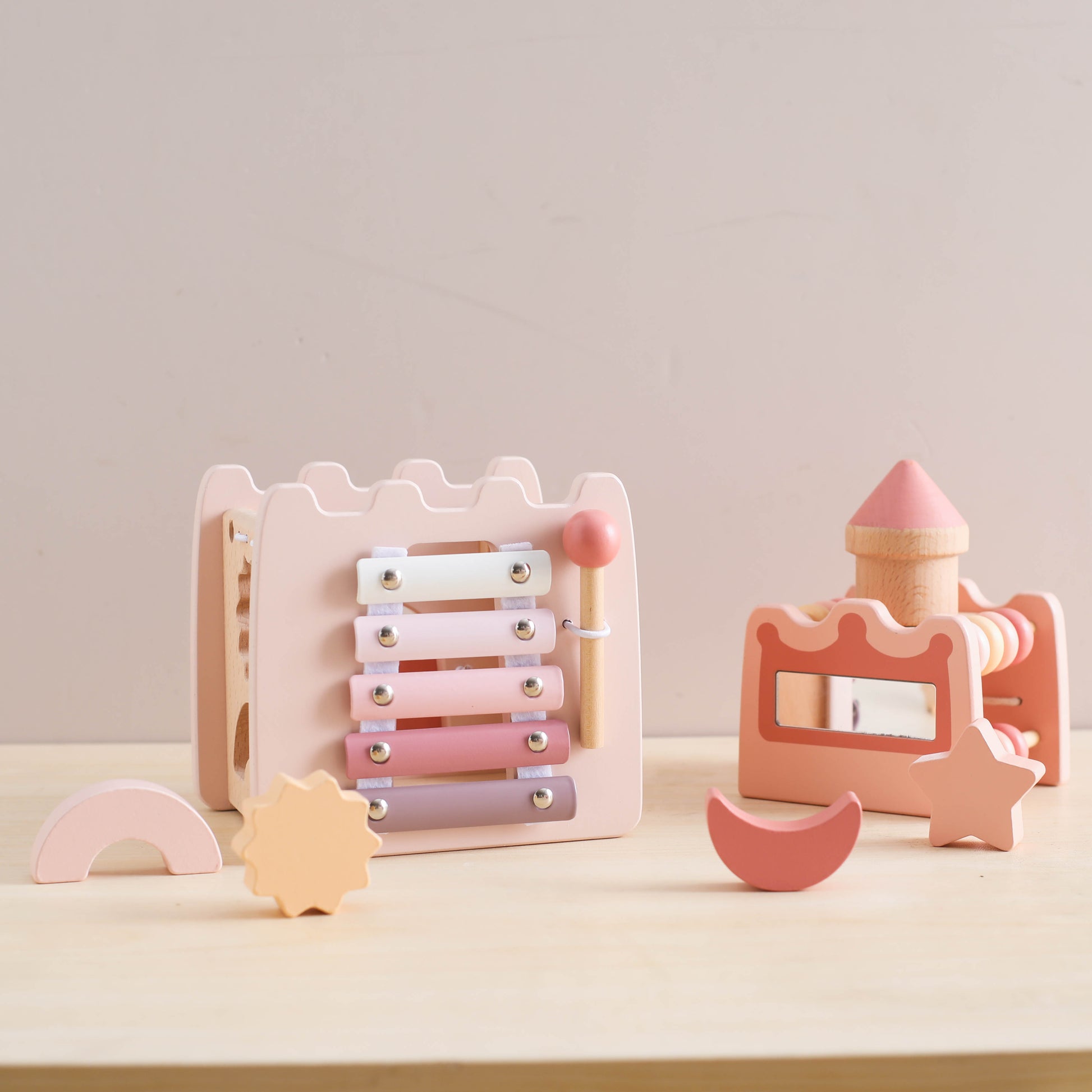 Wooden pink princess castle toy set with xylophone, mallet, and geometric shapes on light table.