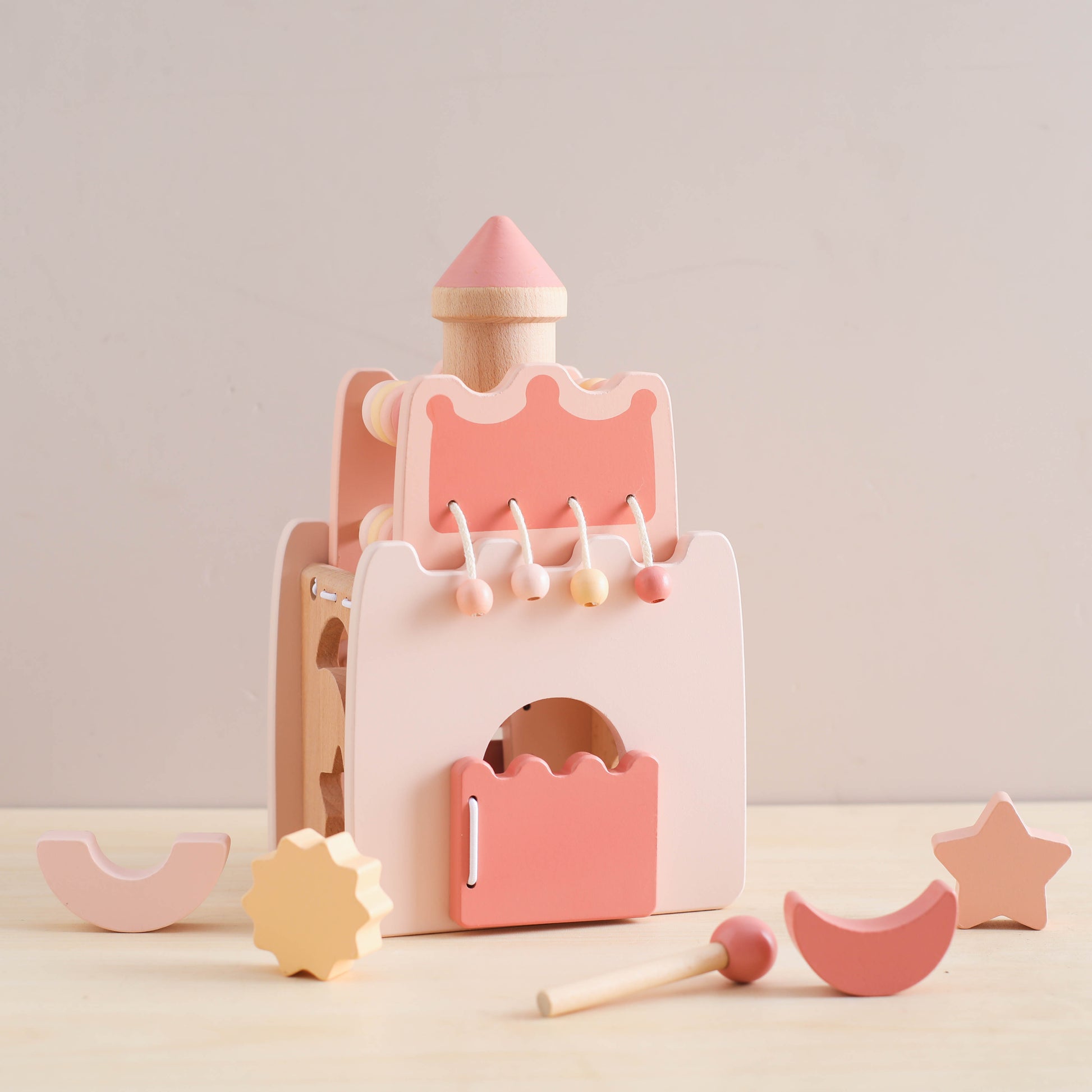 Pink and peach wooden princess castle toy with removable geometric shapes and a small wand accessory.