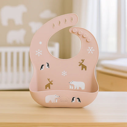 Pink silicone baby bib with reindeer, polar bear, and snowflake prints and a built-in crumb catcher.