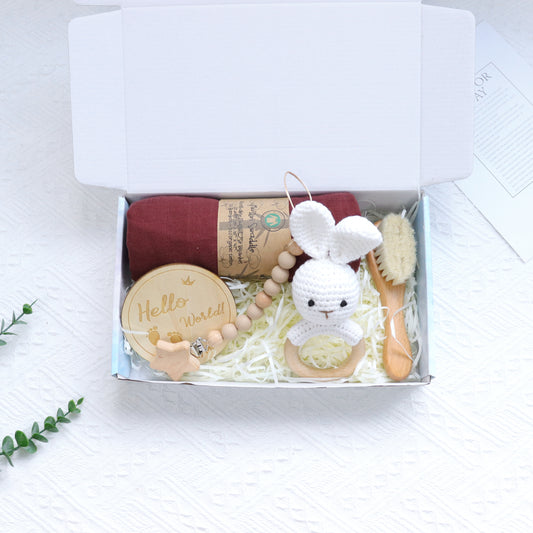 Gift box with baby items including a toy, booties, and a bottle brush on a white background
