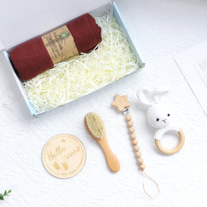 Baby gift set with maroon swaddle, wooden brush, star bead pacifier clip, bunny teether, and wooden "Hello" plaque in box.