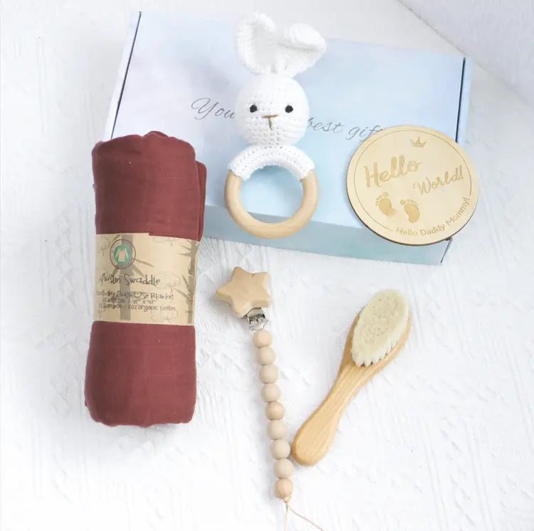 Rust-colored swaddle, wooden hairbrush, beaded pacifier clip with wooden star, white crochet rabbit teether, and round.