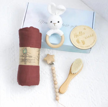 Rust-colored swaddle, wooden hairbrush, beaded pacifier clip with wooden star, white crochet rabbit teether, and round.