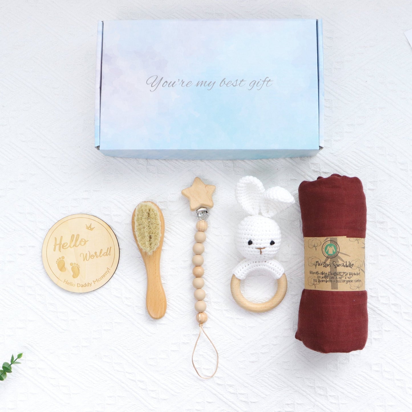 Gift set with wooden baby brush, star-shaped teether, white rabbit rattle, burgundy swaddle, and pastel blue gift box.