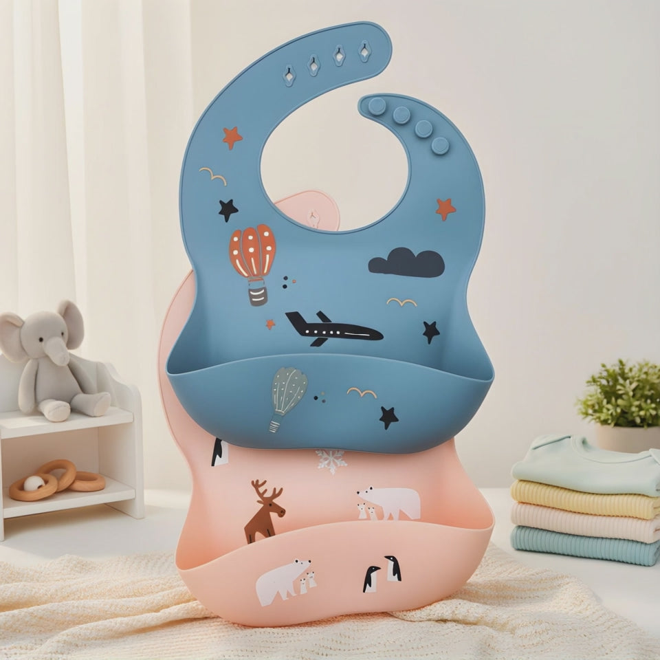 Light blue and Pink silicone bib with airplane, hot air balloon, and cloud designs on a wooden surface.