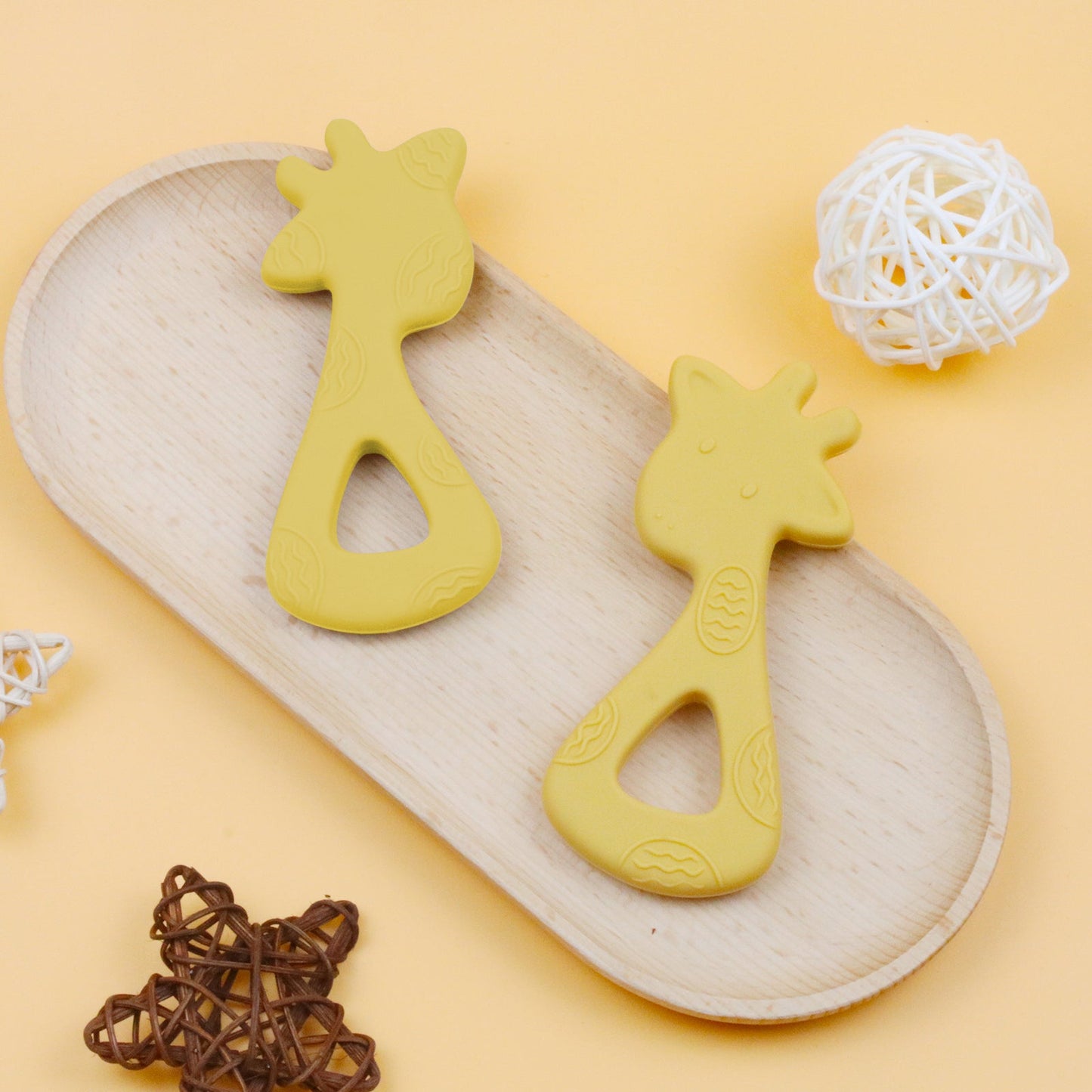 Yellow giraffe-shaped silicone teether with textured details on light wooden tray.