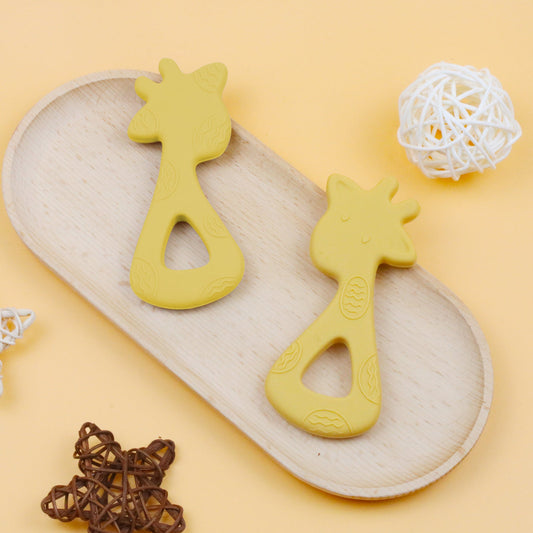 Yellow giraffe-shaped silicone teether with textured details on light wooden tray.