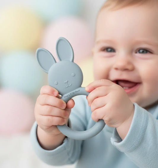 Blue silicone rabbit-shaped teether held by smiling baby in light blue outfit.